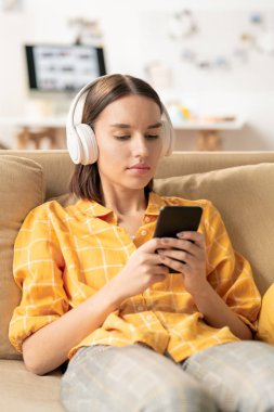 Boş zamanlarında dinlemek için şarkı seçerken akıllı telefonda çalma listesi ne bakarak kulaklık ile Sevimli genç kız
