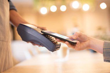 Kafe nin garsonu tarafından tutulan elektronik ödeme makinesinin tuş takımının yakınında akıllı telefonunu tutan genç iş kadını