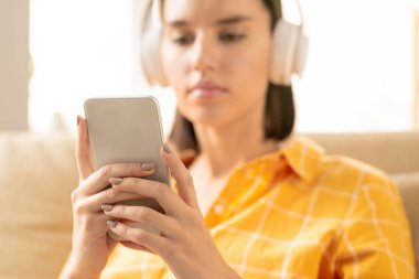 Çalma listesinde gezinirken veya mesajlaşırken akıllı telefonu tutan kulaklıklı genç çağdaş kadının elleri