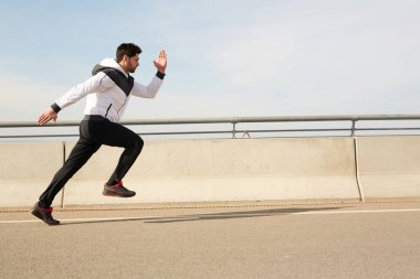 Spor rüzgarlığı ve siyah pantolonlu genç sporcu antrenman yaparken ya da yarışmaya katılırken stadyumun sınırında koşuyor.