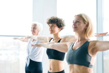 Üç aktif kadın sırası boş zamanlarında çağdaş fitness merkezinde egzersiz yaparken kollarını uzatarak