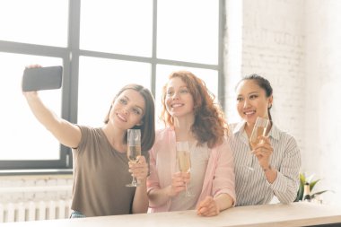 Yaşam etkinliği kutlamaları sırasında şampanya içerken selfie yapan gündelik giyimli üç mutlu kız