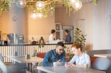 Çağdaş genç çift kafede masa başında oturan, kahve içen ve meraklı videolar için net arama