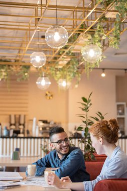 Kafede görev noktaları tartışırken onun kız arkadaşı veya grup arkadaşı bakarak casualwear genç gülen adam