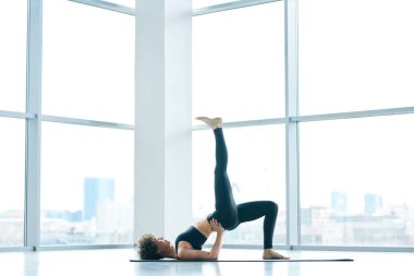 Aktif genç uygun kadın üst sırt üzerinde duran ve katta egzersiz sırasında gerilmiş sağ bacak yükselterek