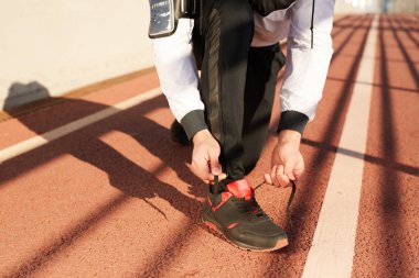 Genç sporcuyu stadyumda koşu müsabakası öncesinde başlangıç çizgisinin önünde spor ayakkabı bağcıkları takarak diz çöktürün
