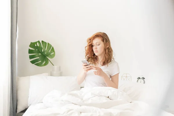 Ξύπνιος Κορίτσι Smartphone Κάθεται Στο Κρεβάτι Υπό Κουβέρτα Και Μηνύματα — Φωτογραφία Αρχείου