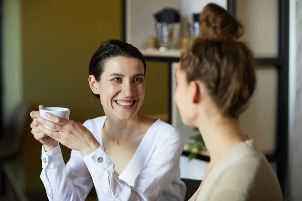 カフェでの会話中に彼女の友人を見てお茶のカップで幸せな若い笑顔の女性 — ストック写真