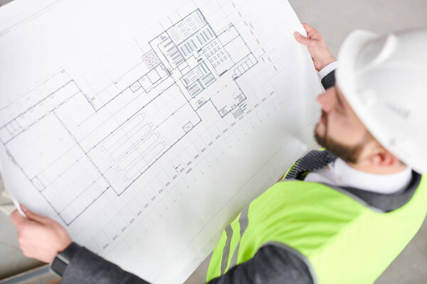 Contemporary engineer looking at construction sketch on blueprint in his hands while working over new project
