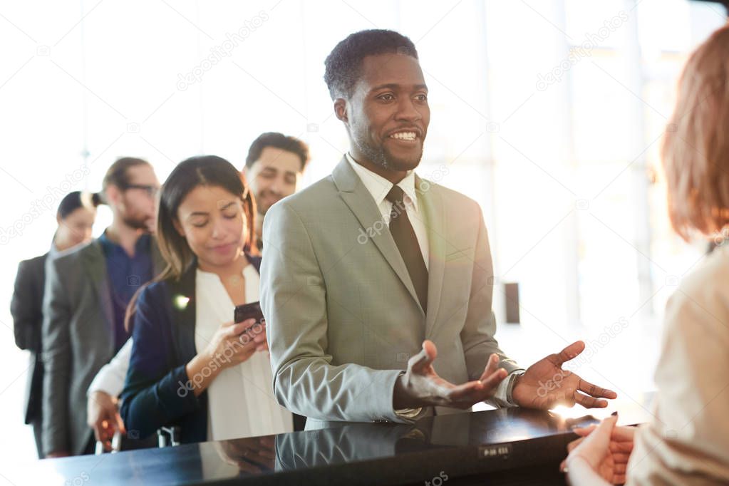 Young elegant business traveler in suit talking to girl by registration counter during check-in before flight