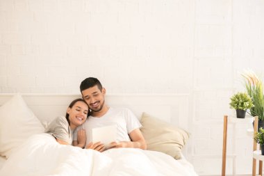 Sabah meraklı video veya film izlerken battaniye altında yatakta yatan genç çağdaş sevgi çift