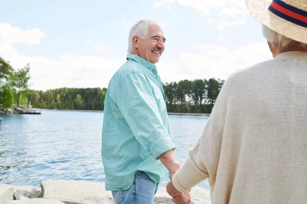 カジュアルウェアで幸せな先輩男性が妻を手で抱きしめ 週末を田舎の湖で過ごす — ストック写真