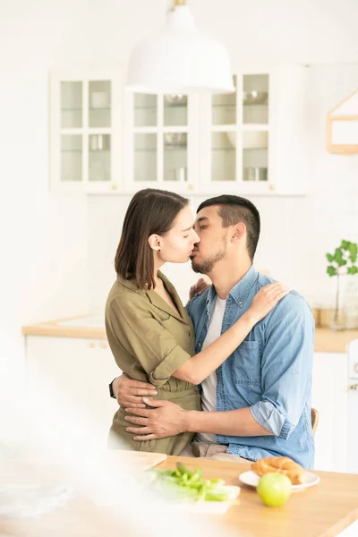 若い不愉美な男は 彼の妻を抱きしめ 両方が提供された台所のテーブルのそばに立っている間 彼女に優しくキスをする — ストック写真