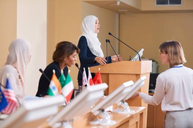 Siyasi konferansta tribün tarafından ayakta dururken başörtüsü ve takım elbise genç çağdaş kadın delege mikrofonkonuşma