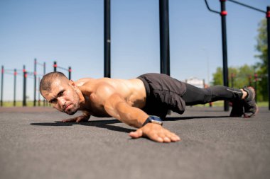 Ağır egzersiz sırasında vücut zemin üzerinde tutarken genç üstsüz vücut geliştirmeci uzanan sol kol