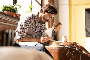 Atölye veya stüdyoda yeni kil öğeleri üzerinde çalışırken çömlek tekerlekleri ile oturan genç çağdaş çömlekçiler küçük bir grup