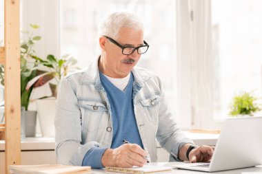 Olgun işadamı veya tasarımcı casualwear notlar yapma ve işyeri tarafından proje hazırlarken net tarama