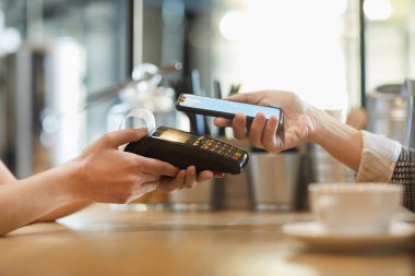 Kafede temassız ödeme sırasında elektronik cihaz ve akıllı telefon ile müşteri ile garson ellerinin yan görünümü
