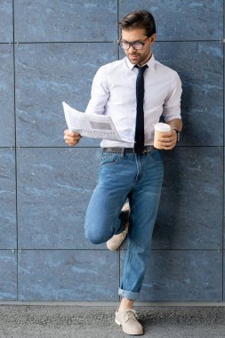 Genç zarif işadamı okuma sözleşme ve kentsel ortamda bina duvar başında dururken içki içen