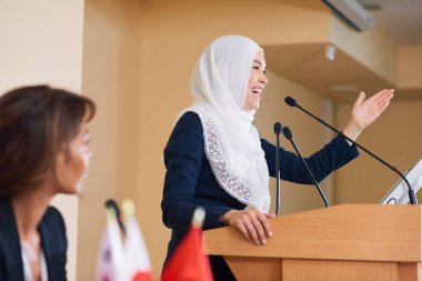 Hijab mutlu genç kadın hoparlör konferansta tribün tarafından ayakta ve seyirci konuşurken gülüyor
