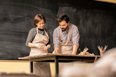 Apron genç erkek çömlekçi toprak tasarımı üzerinde çalışırken onun kadın meslektaşı yeni öğelerden birini gösteren