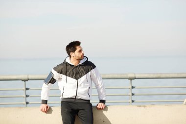 Airpods ve akıllı telefon ile genç çağdaş aktif adam açık egzersiz sonrası dinlenme sırasında müzik dinlerken