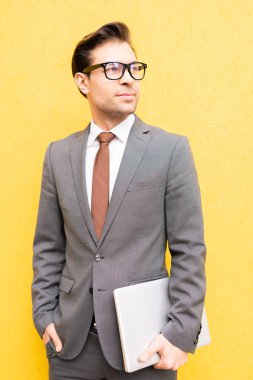 Yalıtım sarı arka plan üzerinde dururken katlanmış dizüstü tutan formalwear ve gözlük genç başarılı işveren
