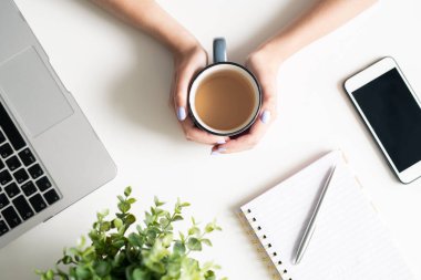 Masa başında otururken ve yeni proje için fikirler düşünürken sıcak çay ile kupa tutan genç kadın elleri üst görünümü