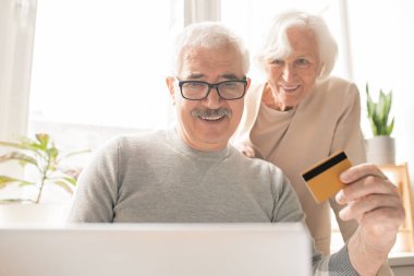 Online alışveriş ve siparişler için ödeme yaparken dizüstü bilgisayar önünde oturan plastik kart ile Çağdaş kıdemli adam