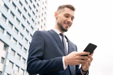İş merkezinin arka planda kentsel ortamda kaydırma cep telefonu ile Mutlu genç zarif işadamı