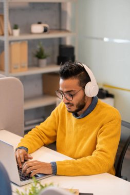 Sakal ve bıyık ile Ciddi genç orta doğu iş stajyer ofiste masada oturan ve müşteri online cevap verirken dizüstü bilgisayar kullanarak