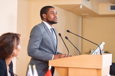 İş arkadaşları veya delegeler için tribün tarafından konuşma yaparken mikrofonda konuşan genç Afrikalı-Amerikalı erkek konuşmacı