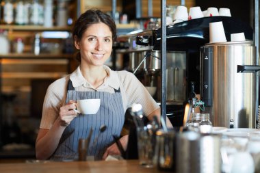 Kafeteryada kahve makinesinin yanında dururken size bakan aromatik içecek fincan ile Pretty genç esmer barista