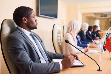 Konferansta yabancı meslektaşlarının arka planda masaya oturan formalwear kendine güvenen genç Afrikalı-Amerikalı delege