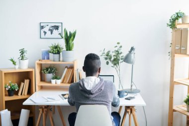 Net bilgi için sörf yaparken duvar önünde masa başında sandalyede oturan kapüşonlu genç kültürlerarası adam Arka görünümü