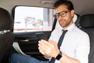 Akıllı casualwear genç kendine güvenen işadamı arabada oturan ve mesajlaşma sırasında akıllı telefon ekranına bakarak