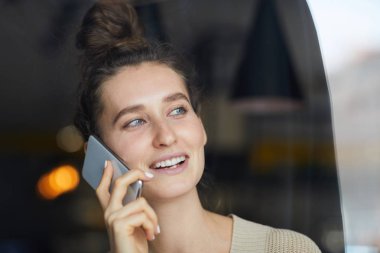 Kafede otururken ve telefon ederken pencereden bakarak gadget ile Mutlu genç mobil iş kadını