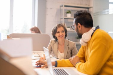 Akıllı rahat kıyafetler içinde olumlu amaçlı genç çok ırklı meslektaşları masada oturan ve açık alan ofisinde birlikte proje üzerinde çalışan