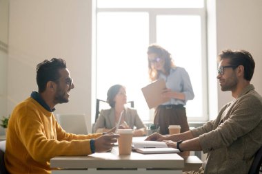 Yeni reklam kampanyasını tartışırken toplantı odasında masada oturan ve fikir paylaşımında bulunan pozitif genç çok ırklı pazarlama uzmanları
