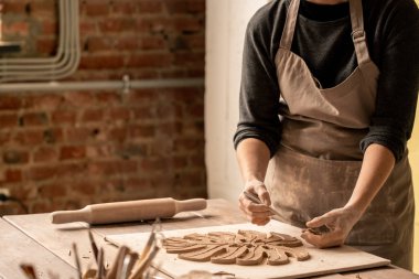 Kilden yaprak şeklini keserken masanın yanında duran çömlekçiliğin genç kadın yaratıcı tasarımcısı