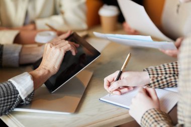 İş arkadaşı veya iş arkadaşları iş düzenlemek için tablet kullanırken kadın çalışanlarından biri not defterine not lar yaparken