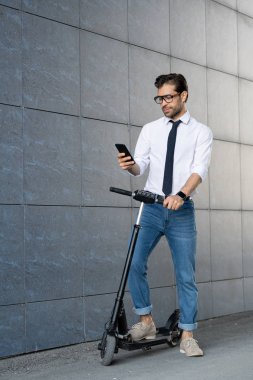Scooter bina duvar boyunca hareket ederken akıllı telefonda kaydırma Çağdaş mobil iyi giyimli çalışan