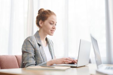 Üniversite projesi üzerinde çalışırken kafede masada oturan ve dizüstü bilgisayar kullanarak damalı ceket li güzel kızıl saçlı öğrenci kız Gülümseyen