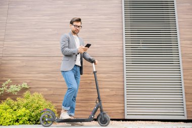 Kentsel ortamda akıllı telefon mesajlaşma sırasında scooter bir bacak tutmak akıllı rahat genç ciddi mobil çalışan