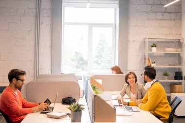 Turuncu kazak lı genç adam kimlik belgesini kontrol ederken proje hedeflerini tartışan içerik genç iş arkadaşları