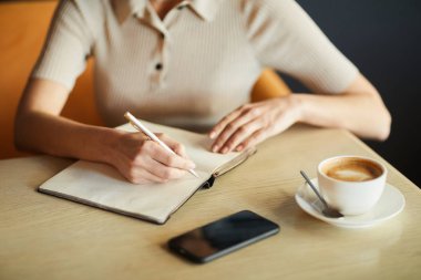 Kahve molasında kafede masa başında otururken dizüstü bilgisayarda iş planı üzerine notlar alan akıllı gündelik genç iş kadını