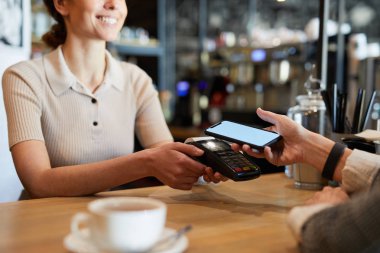 Elektronik ödeme makinesi tutarken bar sayacı tarafından duran ve içecek için ödeme akıllı telefon ile müşteri beklerken genç garson