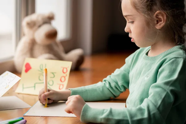 緑のセーターの真剣なかわいい女の子は テーブルに座って 彼女の部屋で父親のためのフェルトペンで絵を描きます — ストック写真