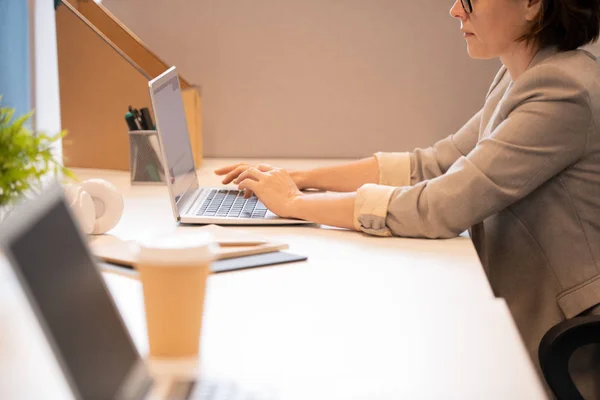 電子メールキャンペーンを構築しながら 机に座ってラップトップに入力するジャケットで深刻な忙しい女性のクローズアップ — ストック写真
