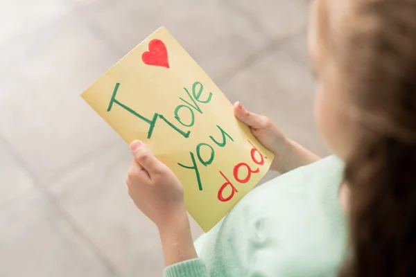 Close-up of unrecognizable little daughter holding handmade postcard for father while preparing to make surprise